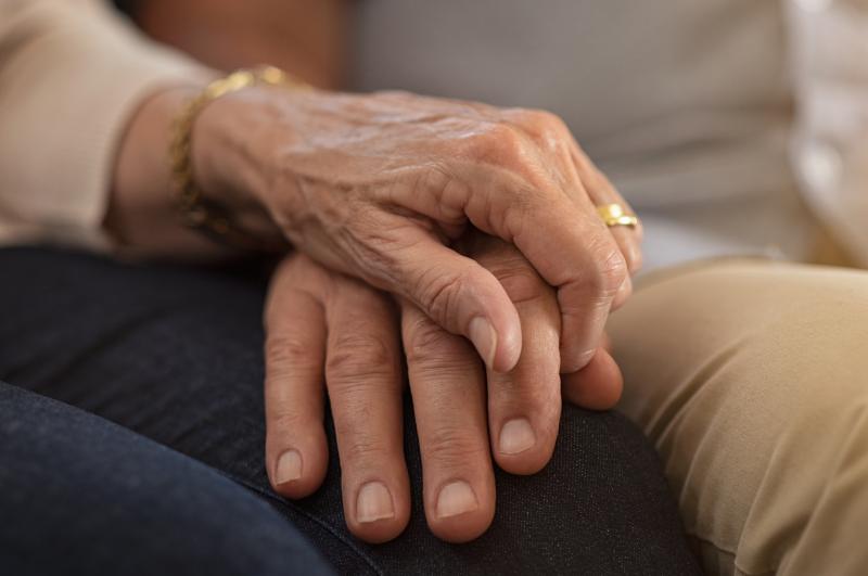 a photograph shows an older couple sat closely, holding hands