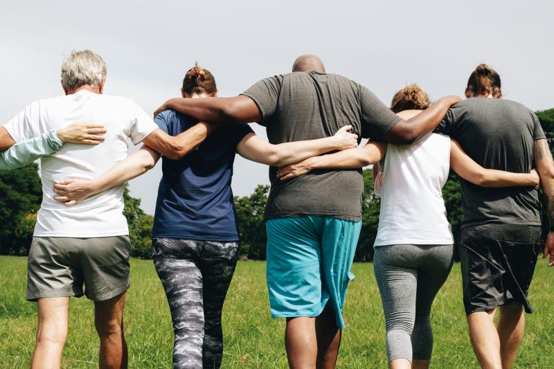 A group of people walking away from the camera with arms on each others shoulders